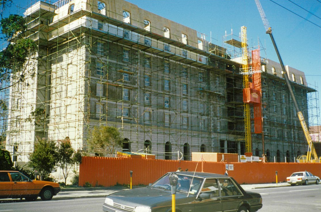 A vintage photo taken from the street of the Hotel Grand Chancellor in Launceston. The exterior of the impressive building is encircled with orange site fencing, scaffolding and a crane operates high above.