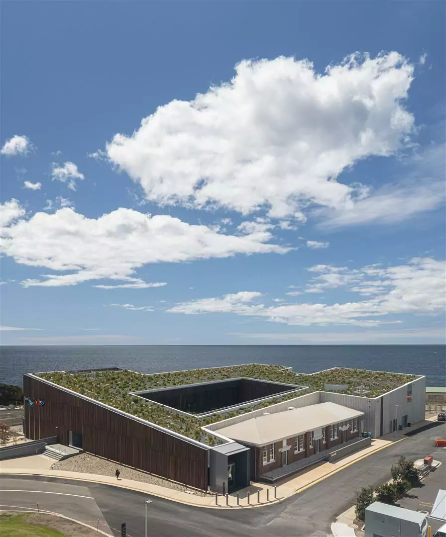 University of Tasmania Cradle Coast Campus, Tasmania. An elevated photo of the Fairbrother project showing the green roof feature, with Bass Strait and a blue, clouded sky in the background.