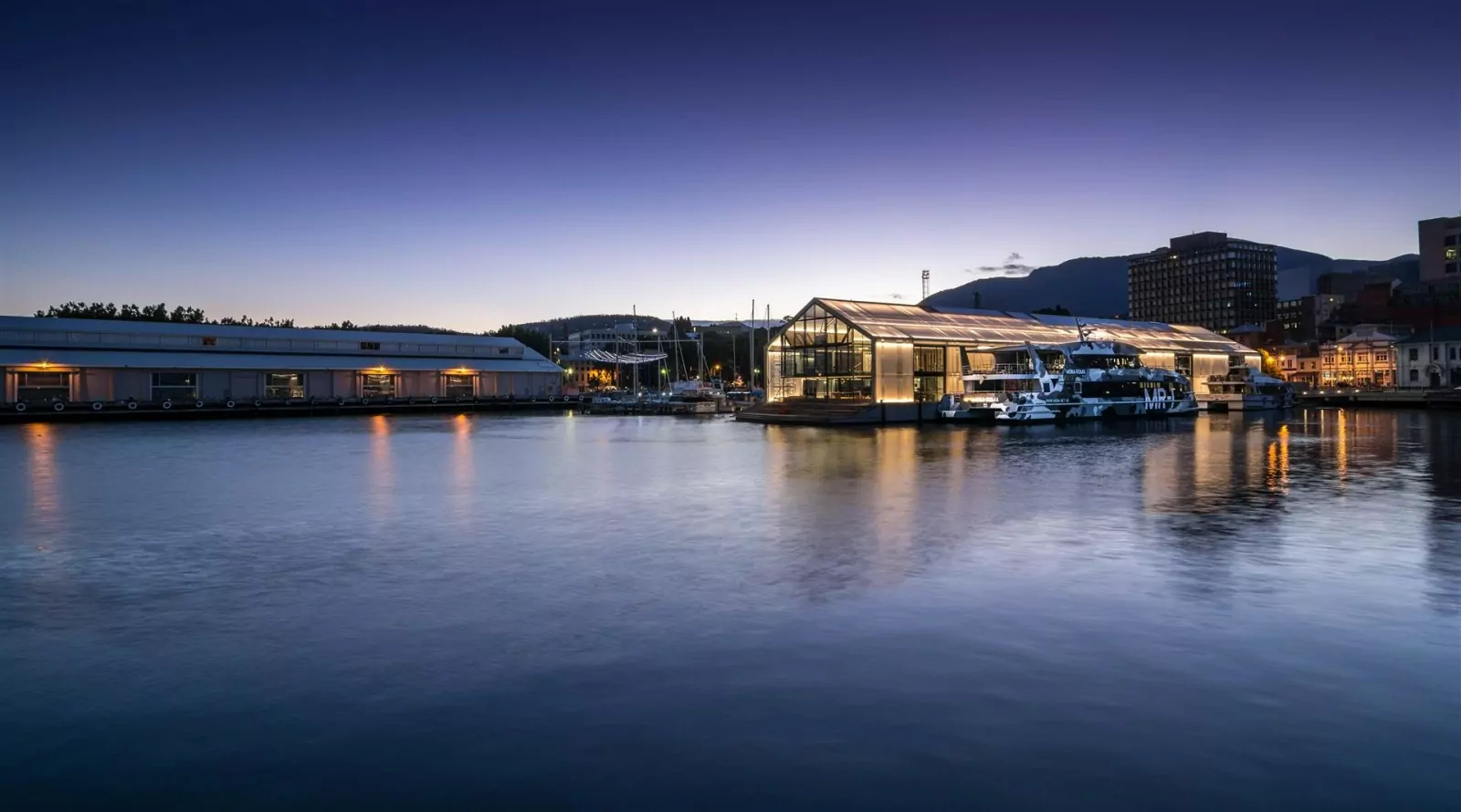 An illuminated three-story ferry terminal superstructure sits on top of a 80m by 20m concrete pontoon above the nighttime Hobart waterfront.