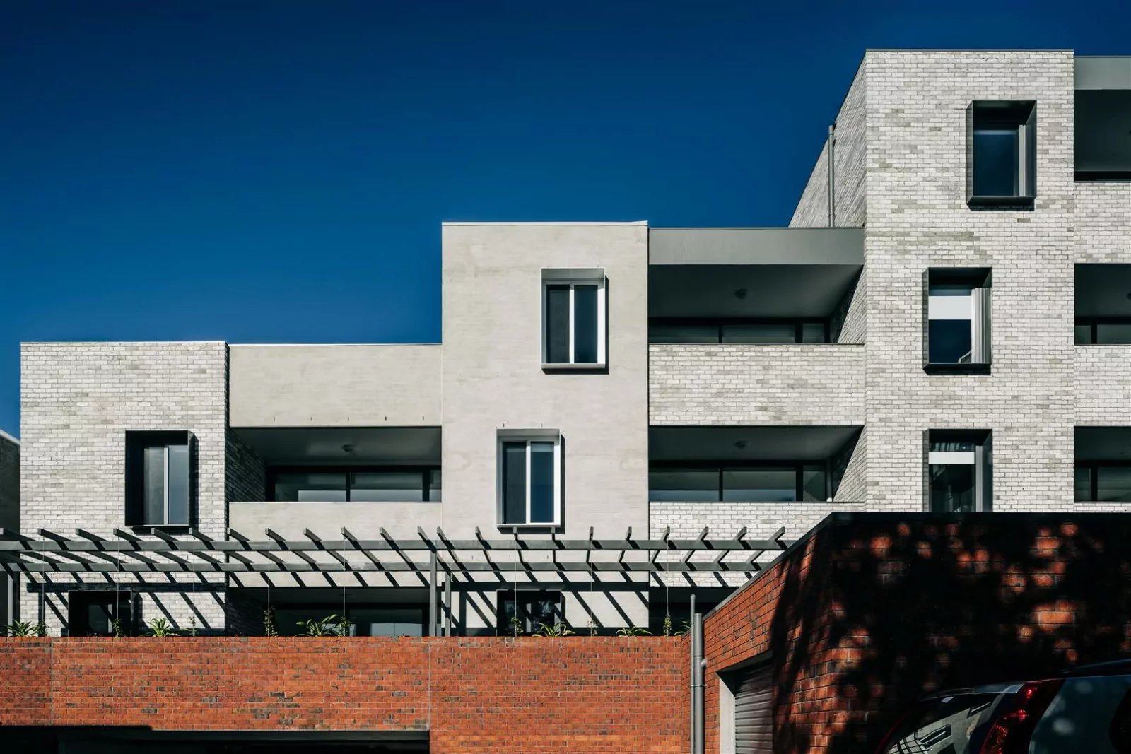 A streetview photo of the 5-storey Goulburn Street Apartments. The Communities Tasmania apartments are designed to house at-need residents over the age of 50. The building's white brick wall external façade provides a nice contrast to the traditional brick wall in the foreground and the clear blue sky.