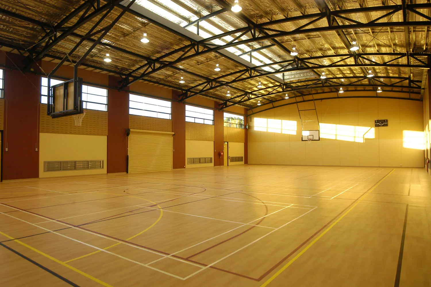 The multi-sport indoor courts of the Girton Grammar Gymnasium. The court is finished with Gerfloor vinyl and line marking for 13 different court configurations. Sunlight shines warmly through the gym windows against the backwall of the gym.
