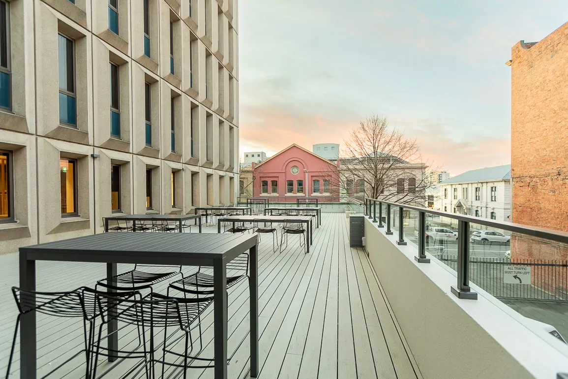 A vibrant sunset lights up the neighbouring brickwork next to the patio of the refurbished Hydro Tasmania Level 1. Seven sets of seats and tables are arrayed on the wood floors.