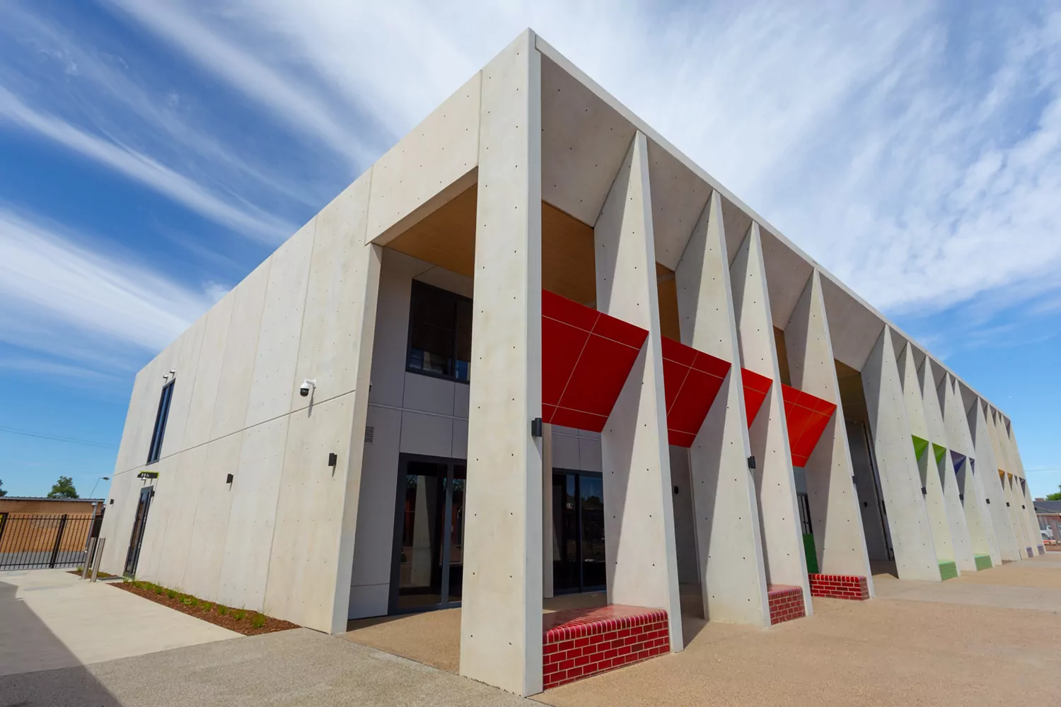 The exterior of a concrete building of the Notre Dame College Arts Centre with vibrant red and green feature brickwork interspersed on the near side.