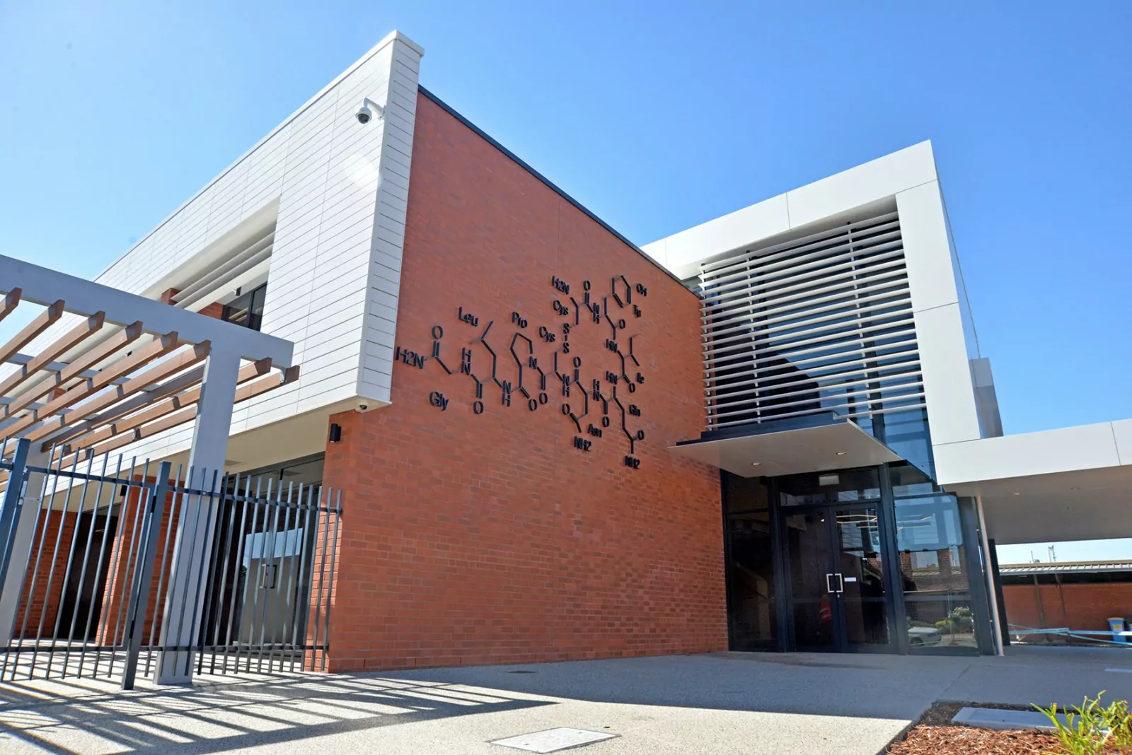 The external façade and entrance of the Jennings and Mungovan Learning Community and Science Centre at Notre Dame College. The redbrick wall has an appropriate fixture of a chemical compound, with surrounding Terracotta European tile and Vitracore G2 alumininum cladding.