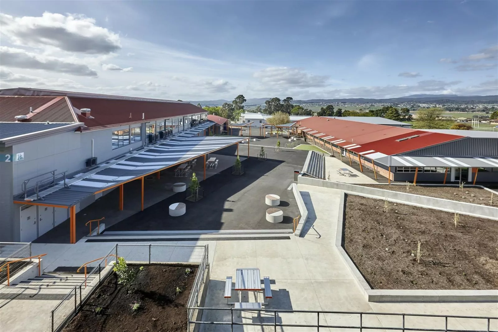 An aerial photo of the redeveloped contemporary, state-of-the-art facilities at Riverside High School. There is timber picnic seating, various concrete pedestrian walkways and two large buildings that extend into the photos distance.