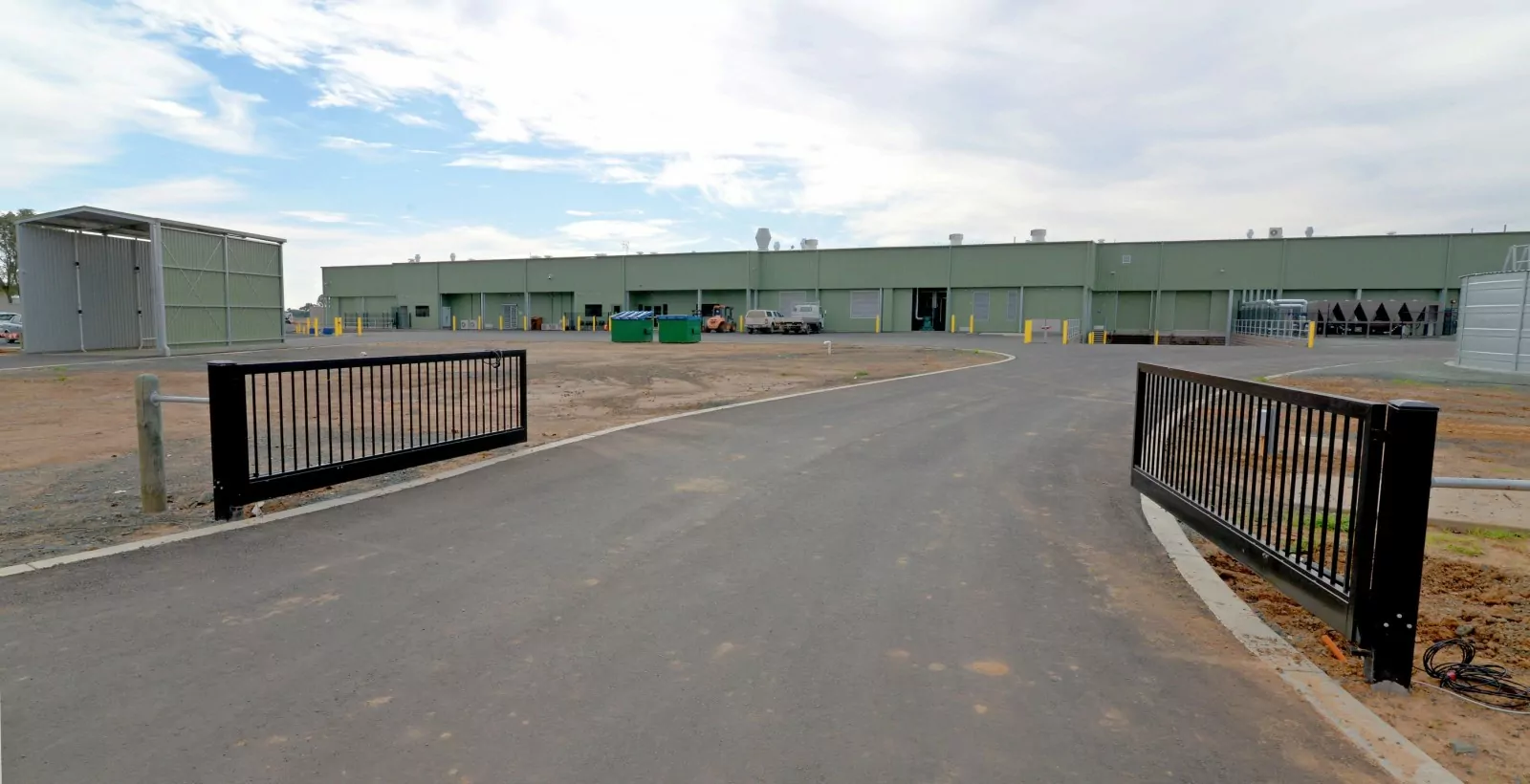 A pair of metal gates marks the start of a wide weathered driveway to the large SBA Chicken Hatchery facility.