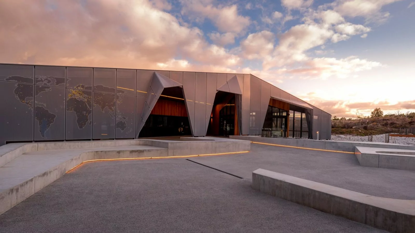 The side profile of the Cradle Mountain Gateway against a sunset. There is a world map painted onto the metal cladding.