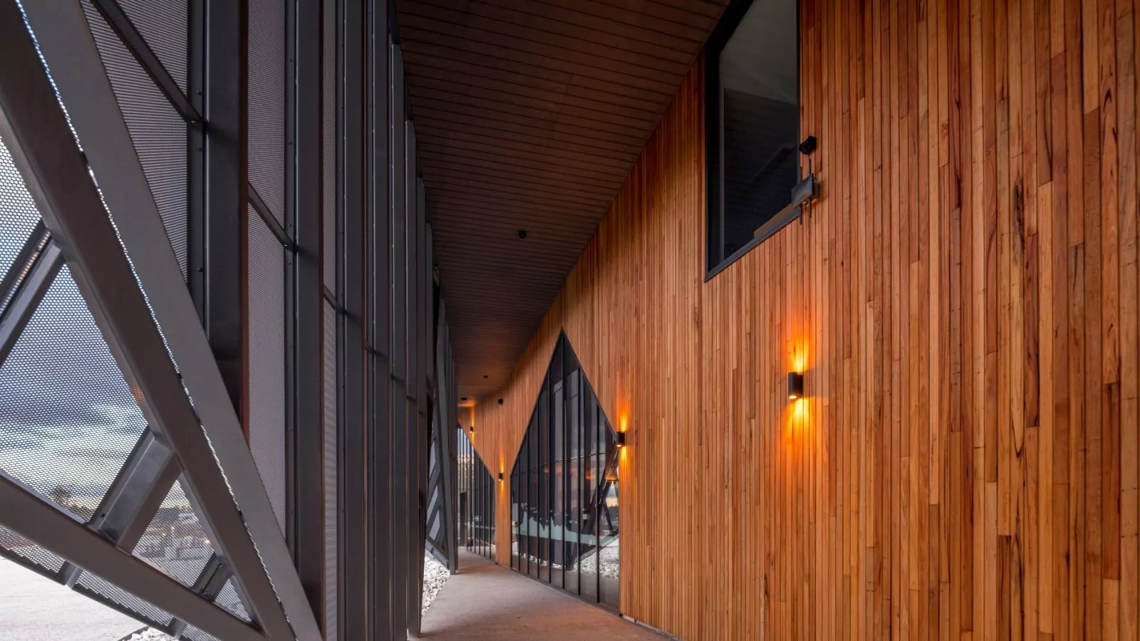 A photo of the wood panels and metal shadings of the Cradle Mountain Gateway. An assortment of wall lights are turned on.