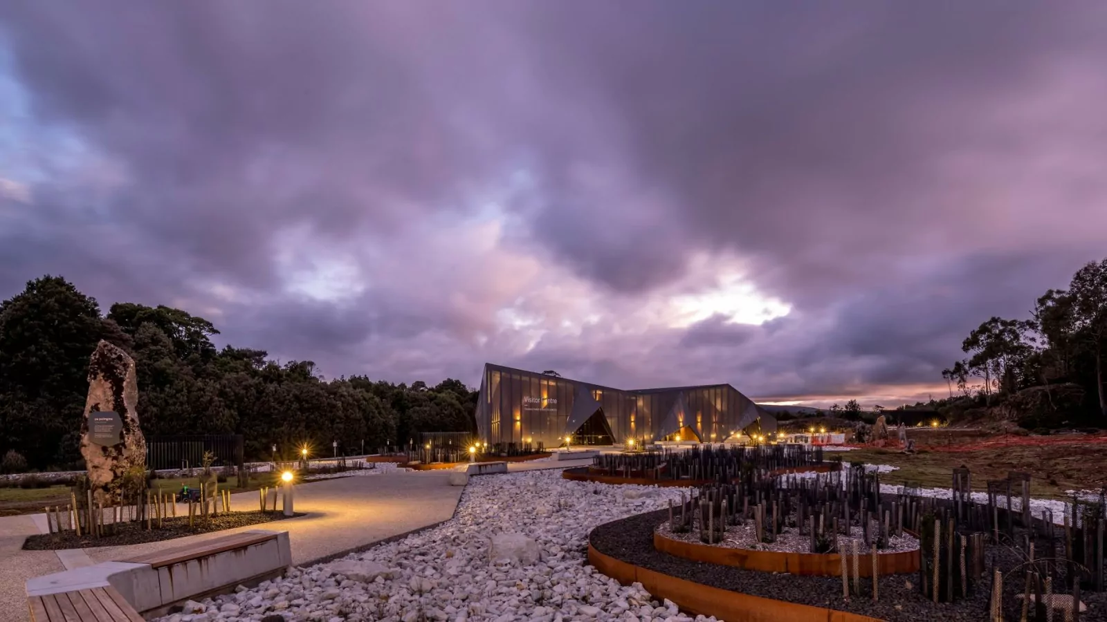 An evening external shot of the Cradle Mountain Gateway building with its concrete walkway. There is extensive native trees surrounding the building.