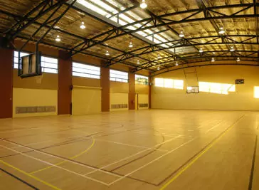 An indoor basketball court with sunlight shine through the windows against one of the backwalls.