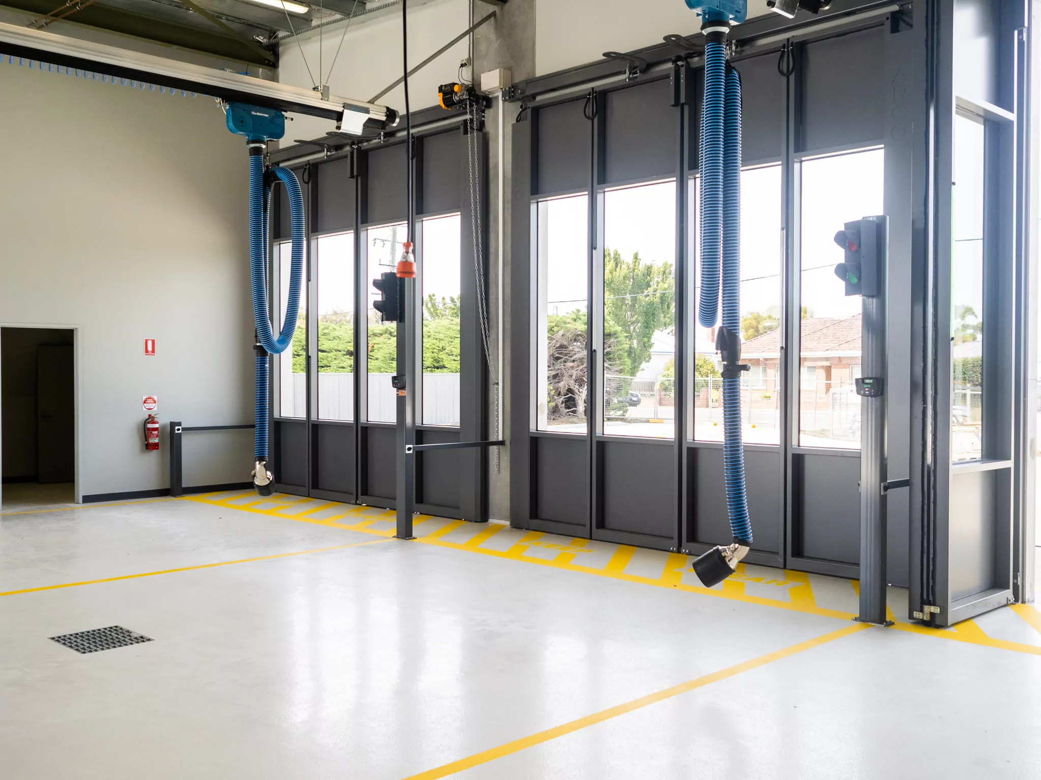 The view from inside the Sorell Emergency Services Hub through the windows of the parking bay doors. Blue ribbed pipes dangle from ceiling fixtures.