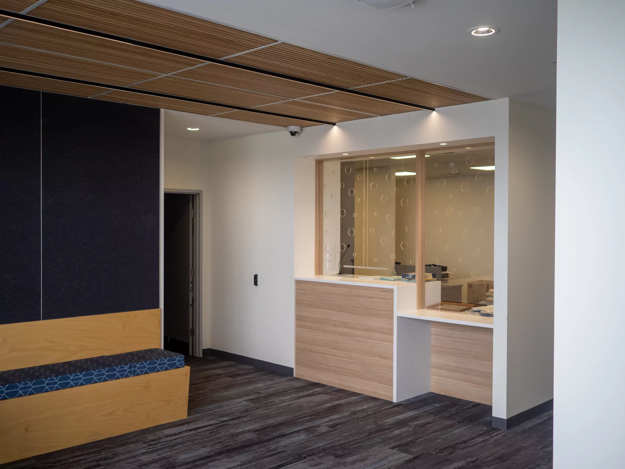 A view of the reception at the Sorell Emergency Services Hub. Timber finishes are visible in the seating, reception desk and ceiling. The Acrylic face shield has holes perforated through it.