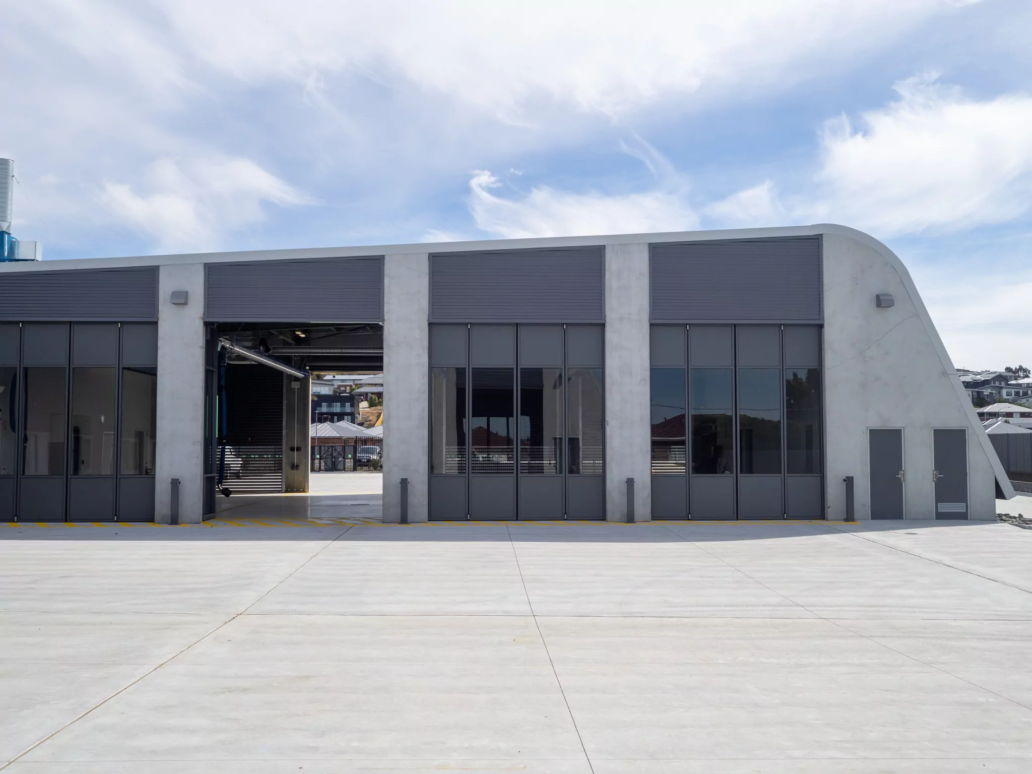 A side profile of the grey slopping concrete building of the Sorell Emergency Services Hub. One of four tall doors are open to the building for emergency vehicles .