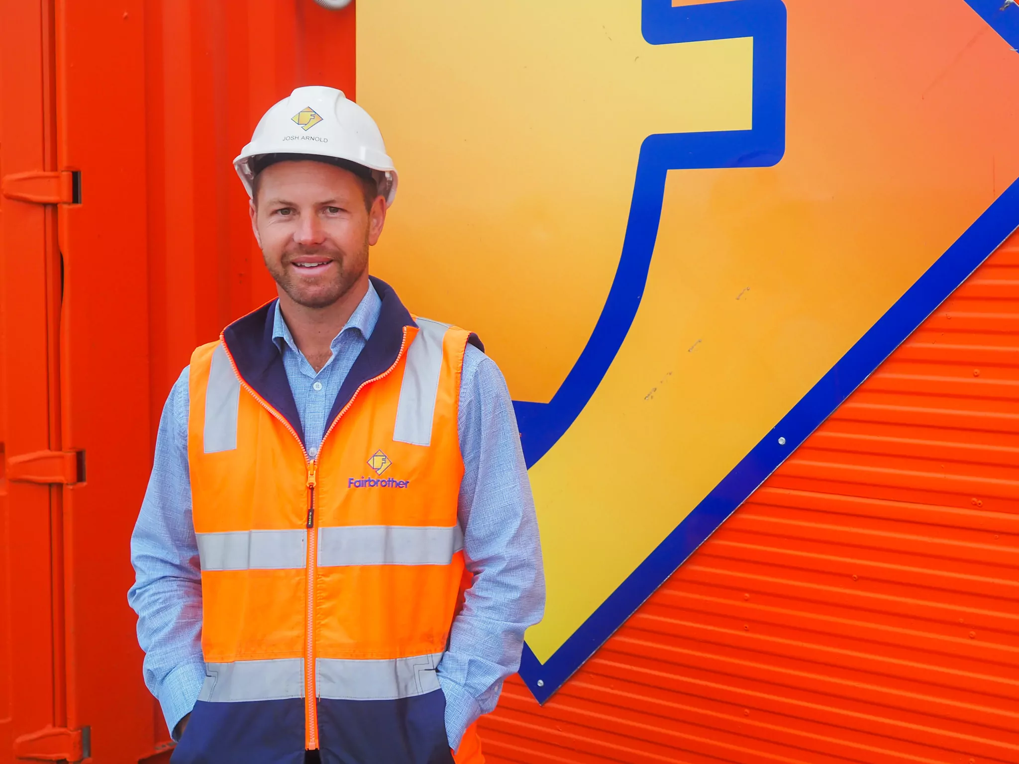 Fairbrother site manager Josh Arnold wearing high vis and hard hat PPE in front of a Fairbrother-branded orange container.